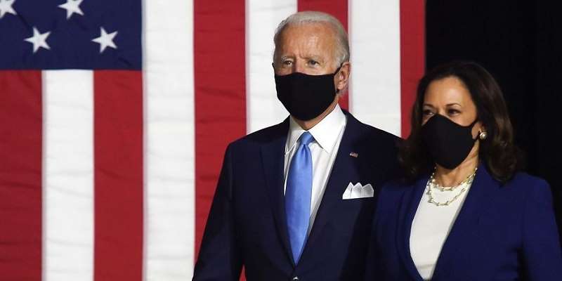 Biden standing next to Harris with face masks on in front of a US flag