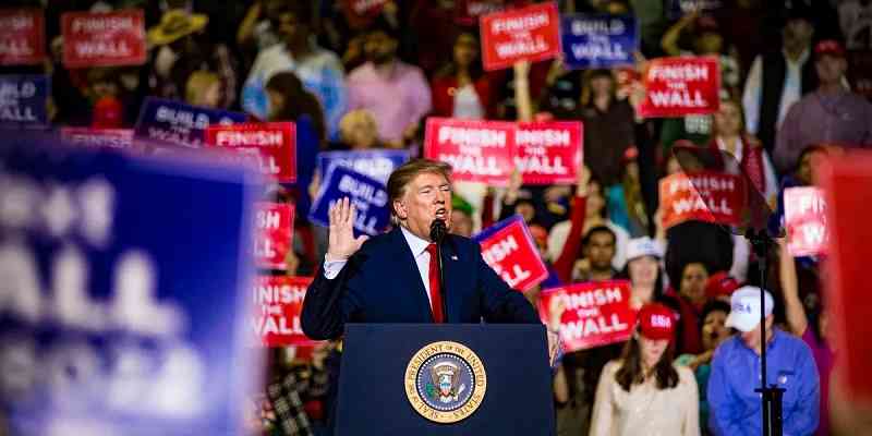 Trump speaking at a podium surrounded by supporters with signs